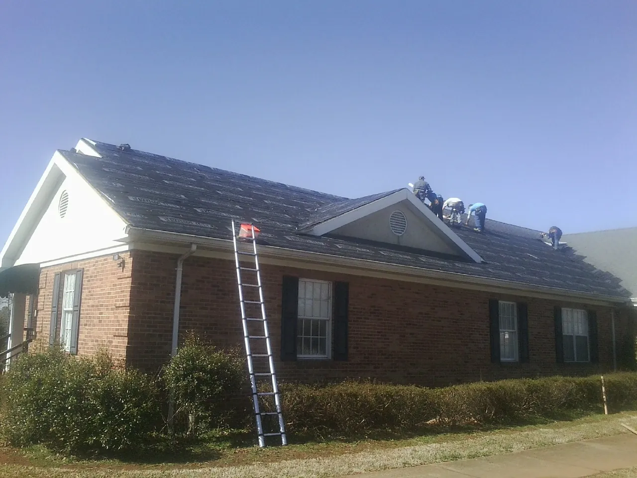 Crew tearing shingles off a brick ranch roof with a ladder set — Metal Roof Repair work by our crew in El Reno