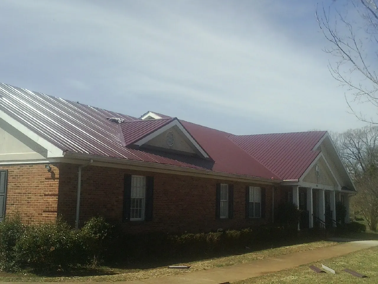 Red metal roof with gabled entries on a long brick building, from a Hail Damage Roof Repair job in El Reno