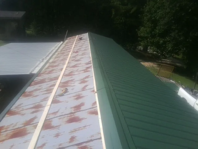 Old rusted panels beside newly installed green metal roofing — Wind Damage Roof Repair by Roofing Brothers in El Reno