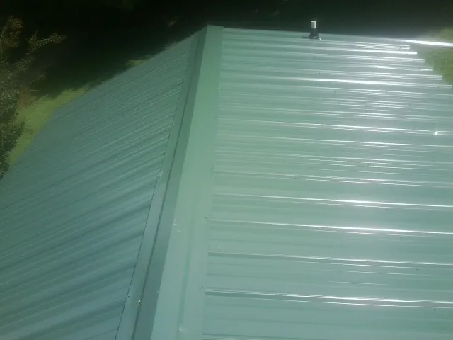 New green metal panels meeting at the ridge of a roof — Flat Roof Repair work by our crew in El Reno