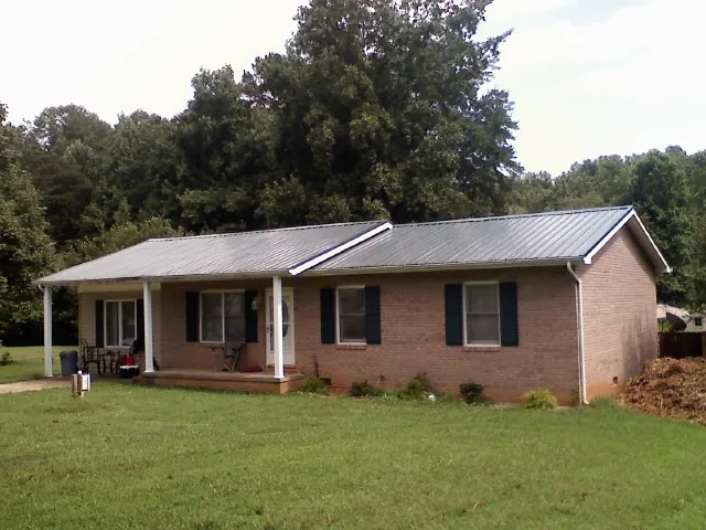 Gray metal roof on a brick ranch house with a side carport in El Reno
