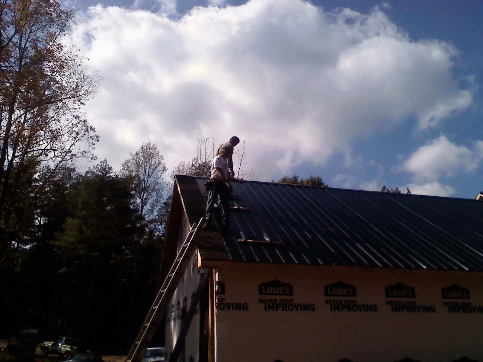 Roofer fastening dark metal panels high against a cloudy sky, from a Roof Inspection job in El Reno
