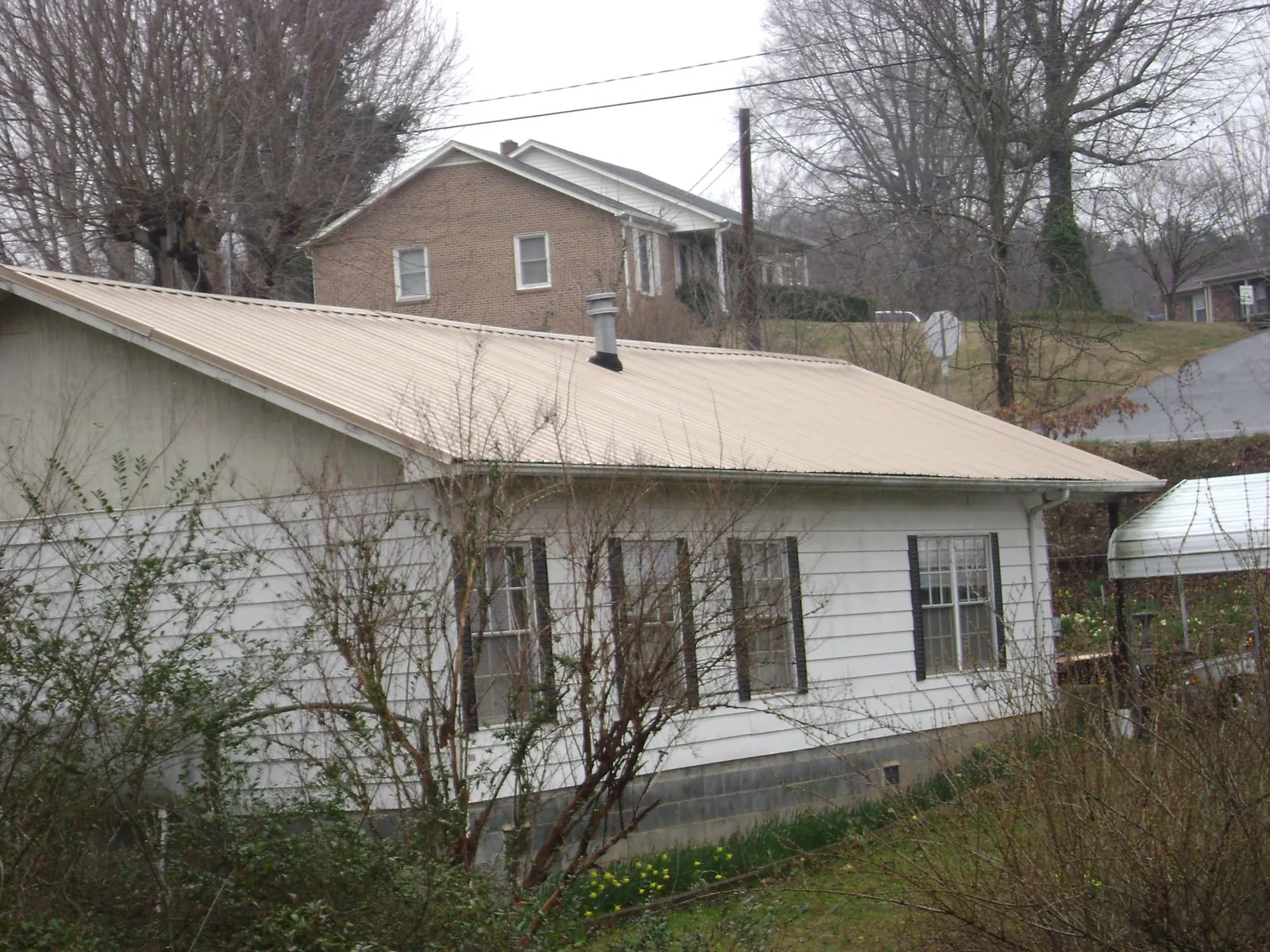 Tan metal roof on a white sided house set into a hillside — Commercial Roofing by Roofing Brothers in El Reno
