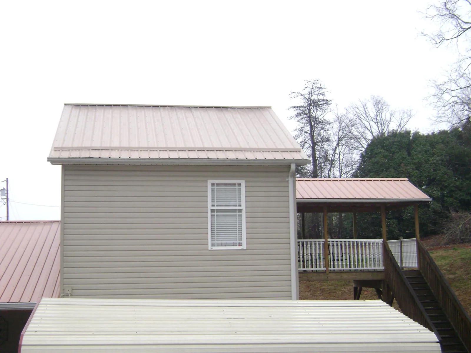 Tan metal roofs on a two story addition and attached porch, from a Roof Replacement job in El Reno